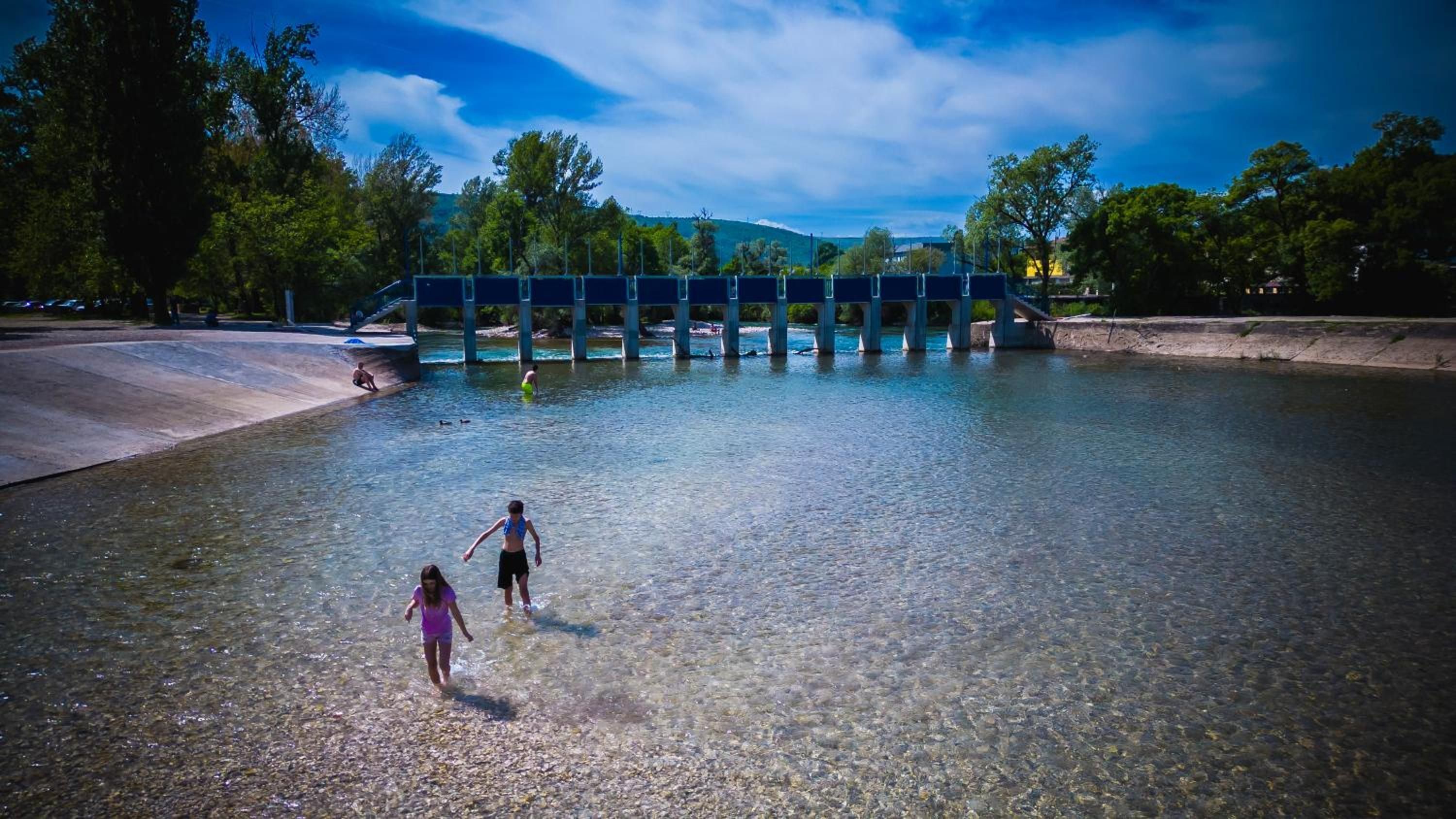 Un plan d’eau aux eaux claires, surmonté d’un pont, entouré d’arbres et bordé d’un paysage vallonné.