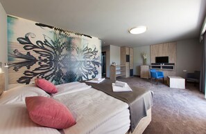 Habitación de hotel con cama, escritorio, silla, televisor y un cuadro abstracto grande en la pared.