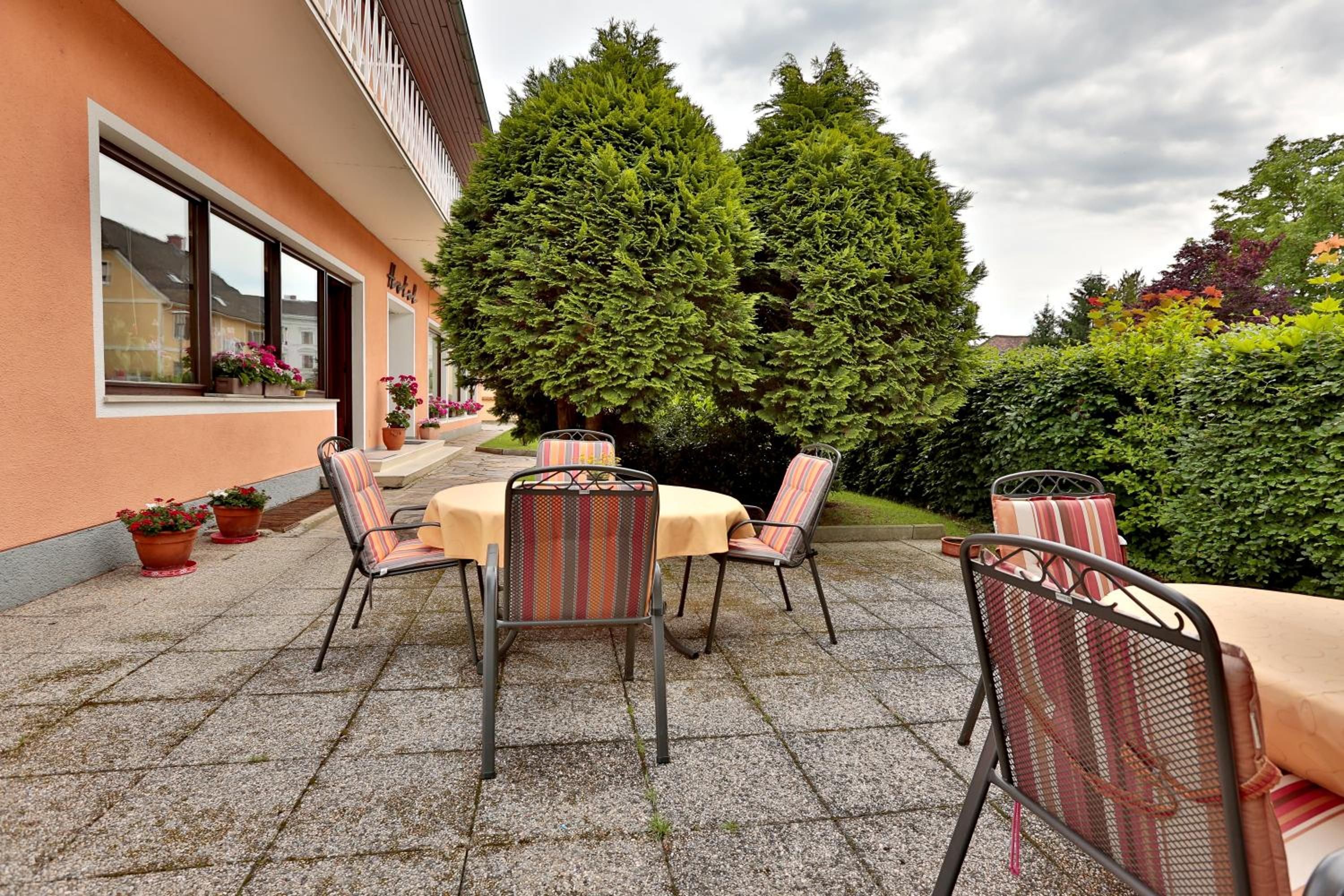 An outdoor patio with tables and chairs, surrounded by potted plants and a large tree.