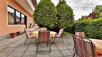 An outdoor patio with tables and chairs, surrounded by potted plants and a large tree.