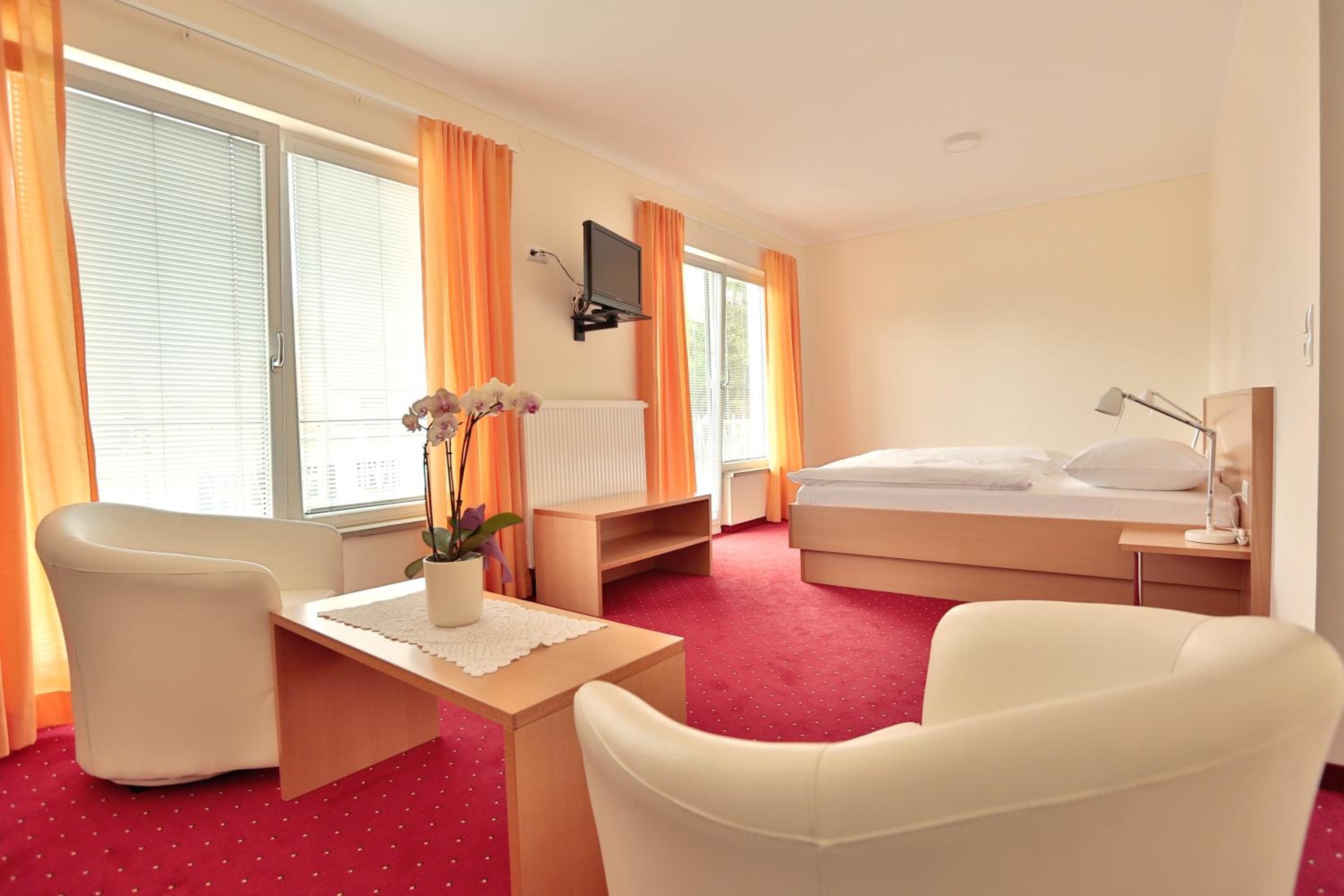 Habitación de hotel con cama, escritorio, silla, televisor y ventana con cortinas.
