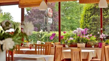 An outdoor dining area with tables and chairs, surrounded by potted plants and flowers.