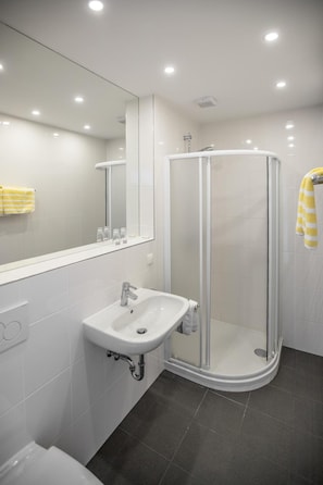 A modern bathroom with a glass-enclosed shower, a white sink, and a mirror above it. - Hotel Reineldis (Mureck)