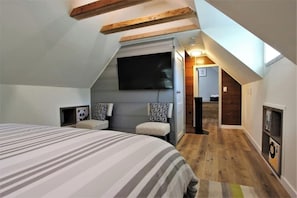 A bedroom with a sloped ceiling, a bed, two chairs, a TV, and a small hallway leading to a bathroom. - The Train Getaway (Big Bear Lake)
