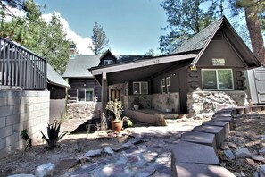 A log cabin with a stone foundation, a covered porch, and a stone retaining wall. - The Train Getaway (Big Bear Lake)