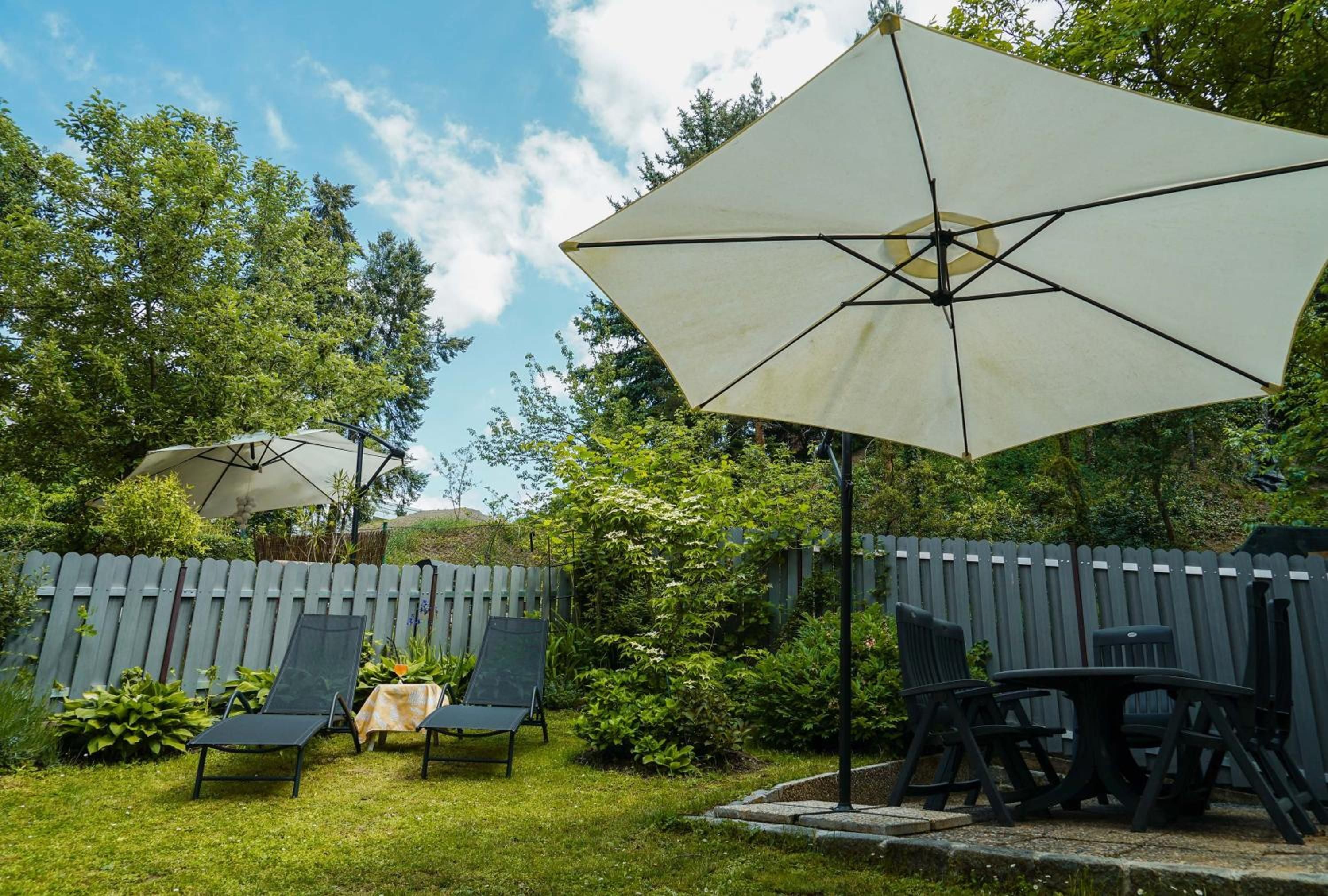 A backyard with a patio area, including a table and chairs, and a large umbrella providing shade.