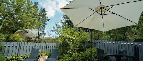 A backyard with a patio area, including a table and chairs, and a large umbrella providing shade.