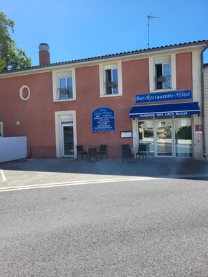 Un edificio con cartel anunciando bar, restaurante y hotel. Hay mesas y sillas en la parte exterior.