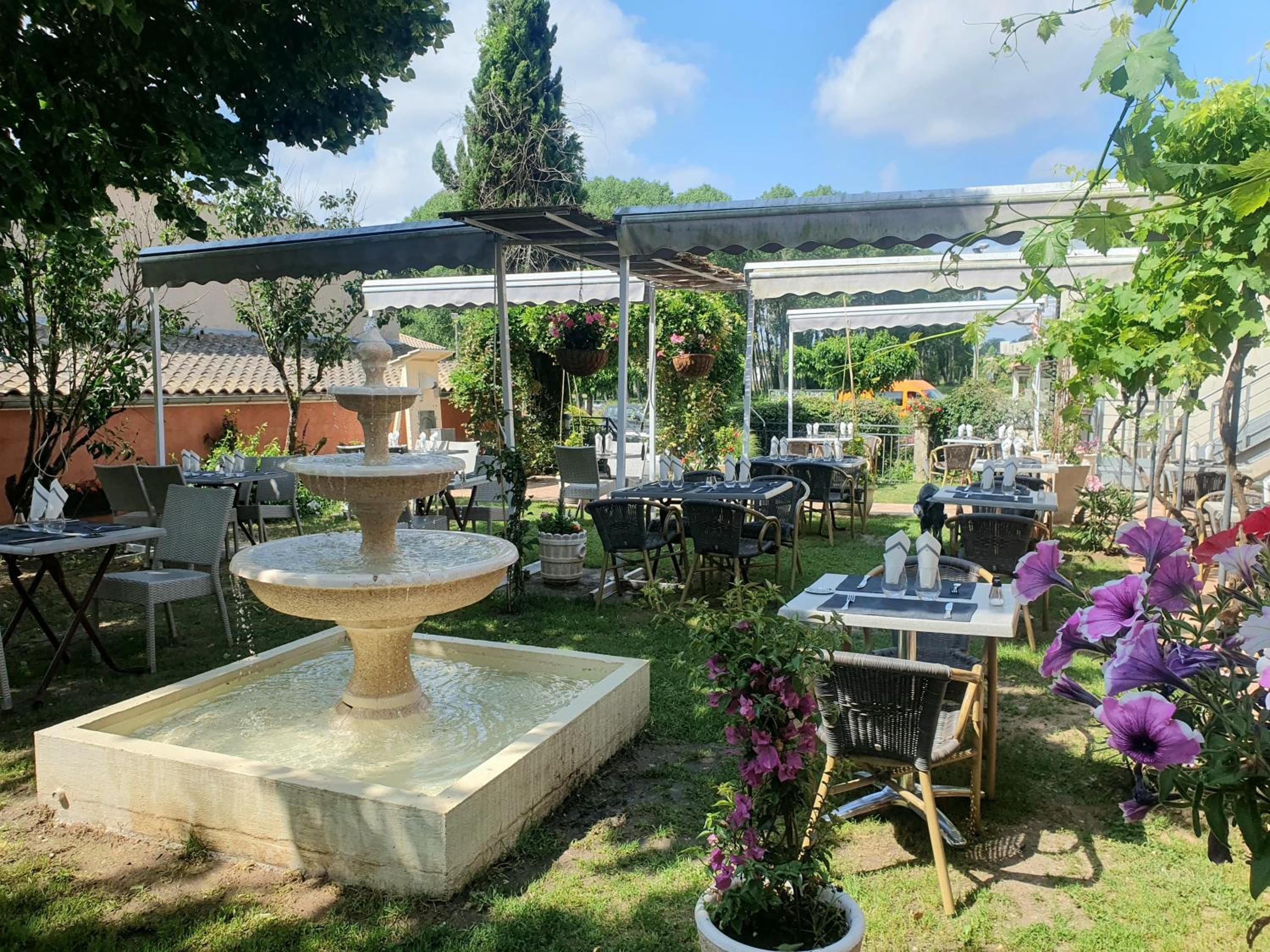 An outdoor patio area with tables and chairs, a central fountain, and potted plants.