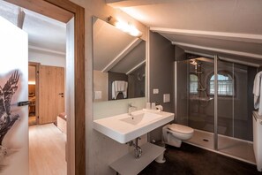 Un baño moderno con un espejo grande, un lavamanos blanco, un inodoro y una ducha con mampara de vidrio.