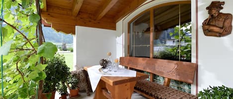 A wooden bench with a carved backrest, a table with a white cloth, and a glass set on the table.