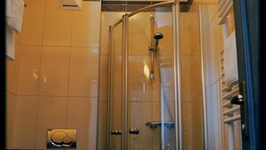 Box de chuveiro com vidro, chuveiro manual, vaso sanitário e porta-toalhas.