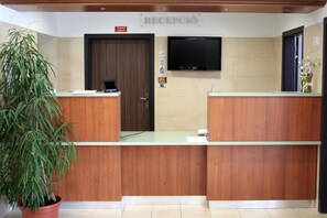 A reception area with a wooden reception desk, a flat-screen TV mounted on the wall, and a potted plant. - Hotel Kelep (Tokaj)