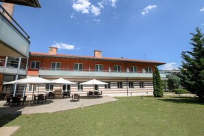 Un edificio con techo plano, varias ventanas y un patio con mesas y sombrillas.