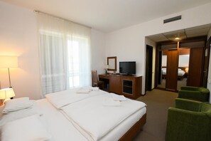 Una habitación de hotel con una cama, un escritorio con televisor, una silla y una puerta que da a otra habitación.
