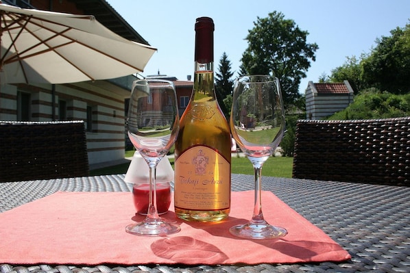 A bottle of Tokaji Aszali wine, two wine glasses, and a pink cloth on an outdoor table.