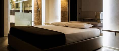 A modern bedroom with a large bed, a glass shower enclosure, and a visible bathroom.