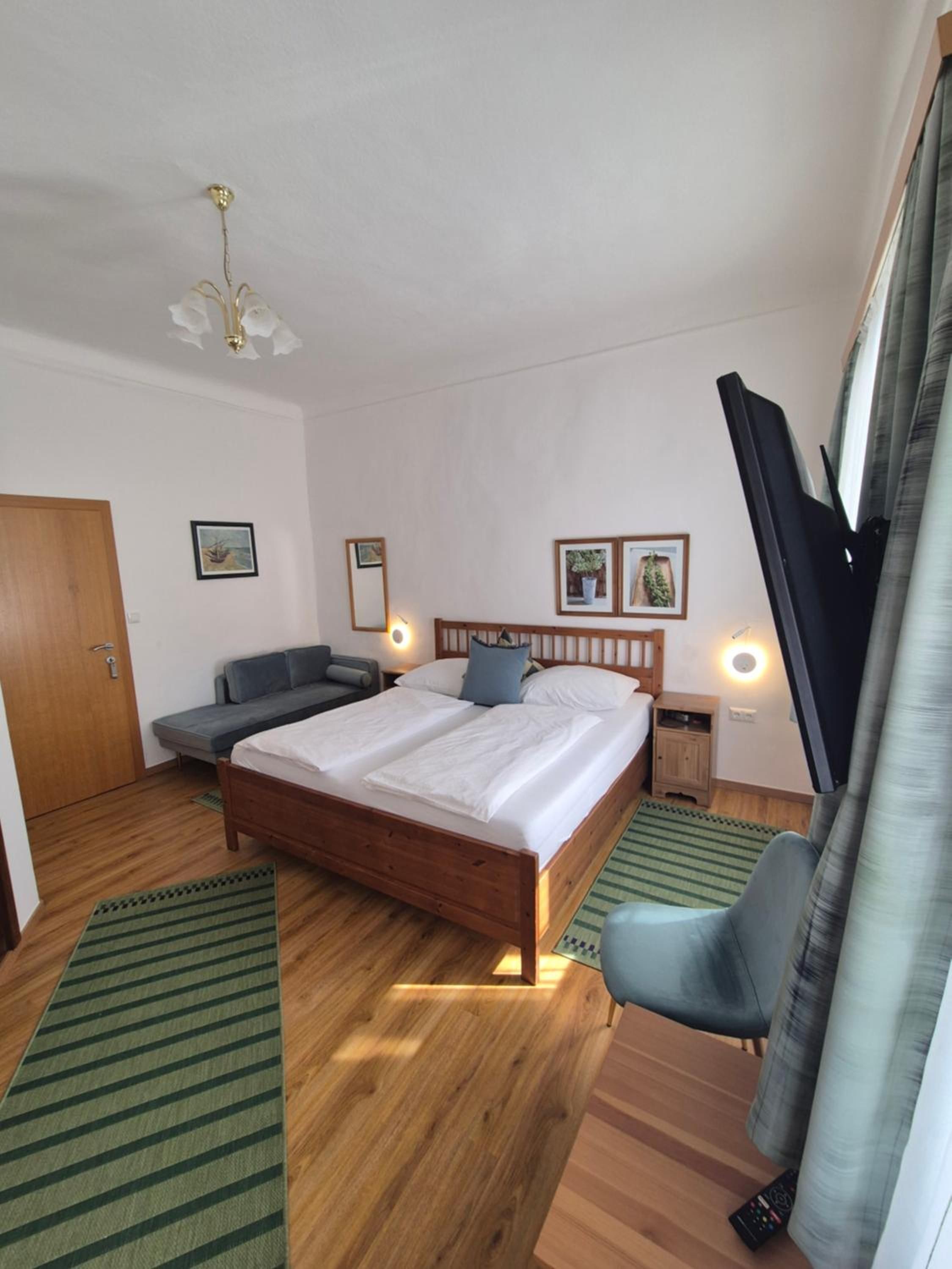A bedroom with a bed, a chair, a TV, and a door.