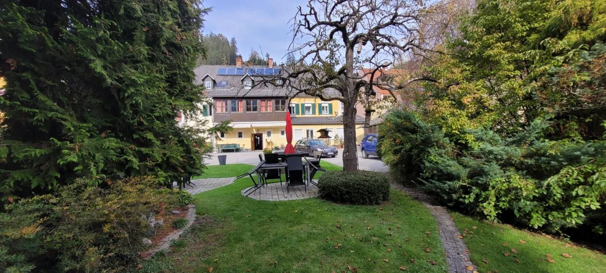 A residential area with a paved pathway, a small round table with chairs, and a building with a yellow facade in the background.