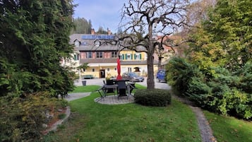 A residential area with a paved pathway, a small round table with chairs, and a building with a yellow facade in the background.