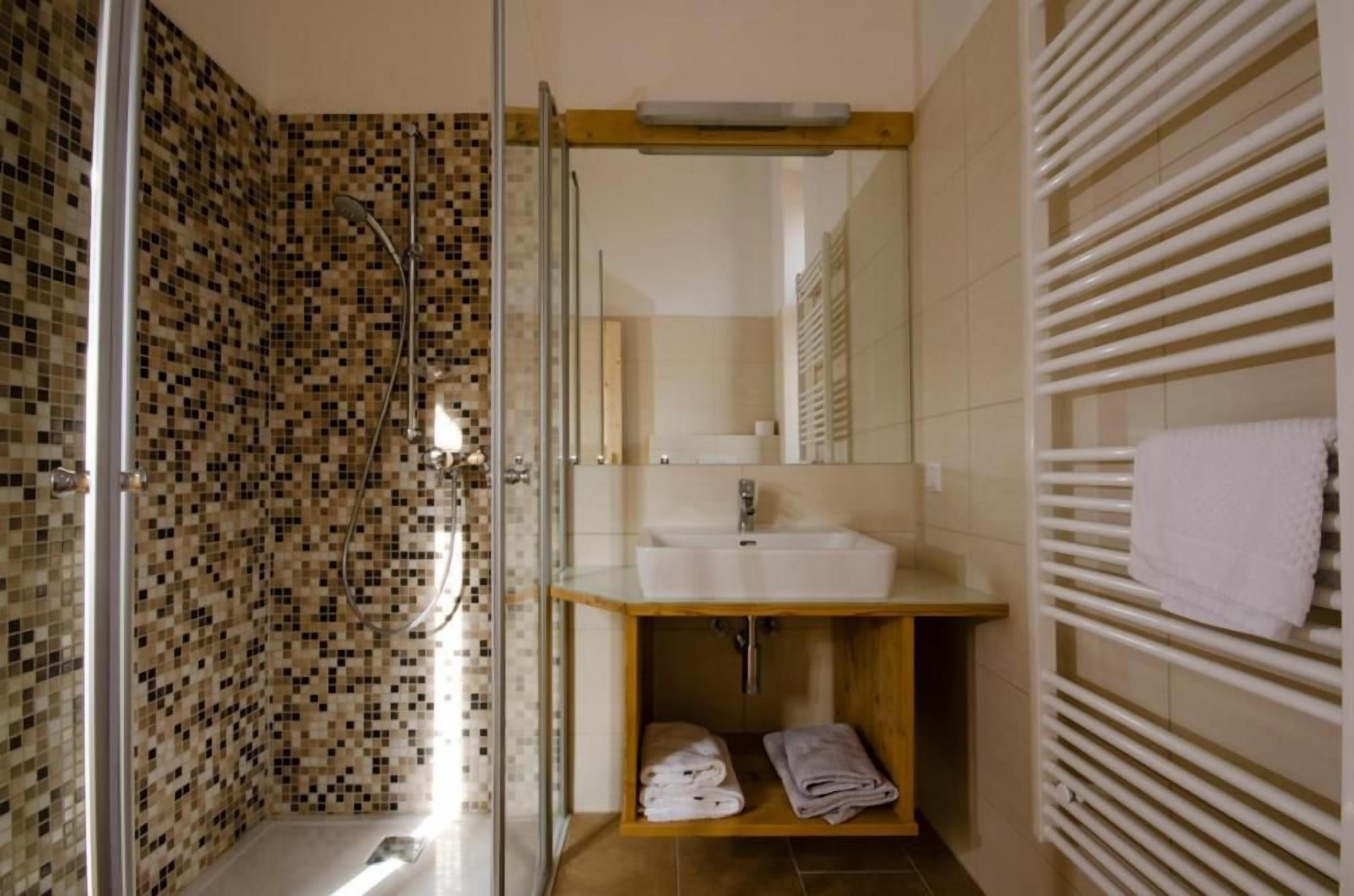 Un baño con ducha envuelta en vidrio, tocador de madera con lavamanos y un perchero para toallas.