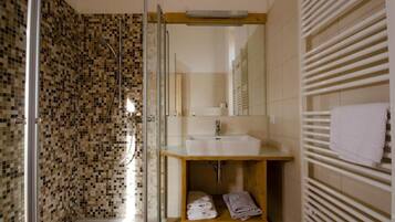 Un baño con ducha envuelta en vidrio, tocador de madera con lavamanos y un perchero para toallas.