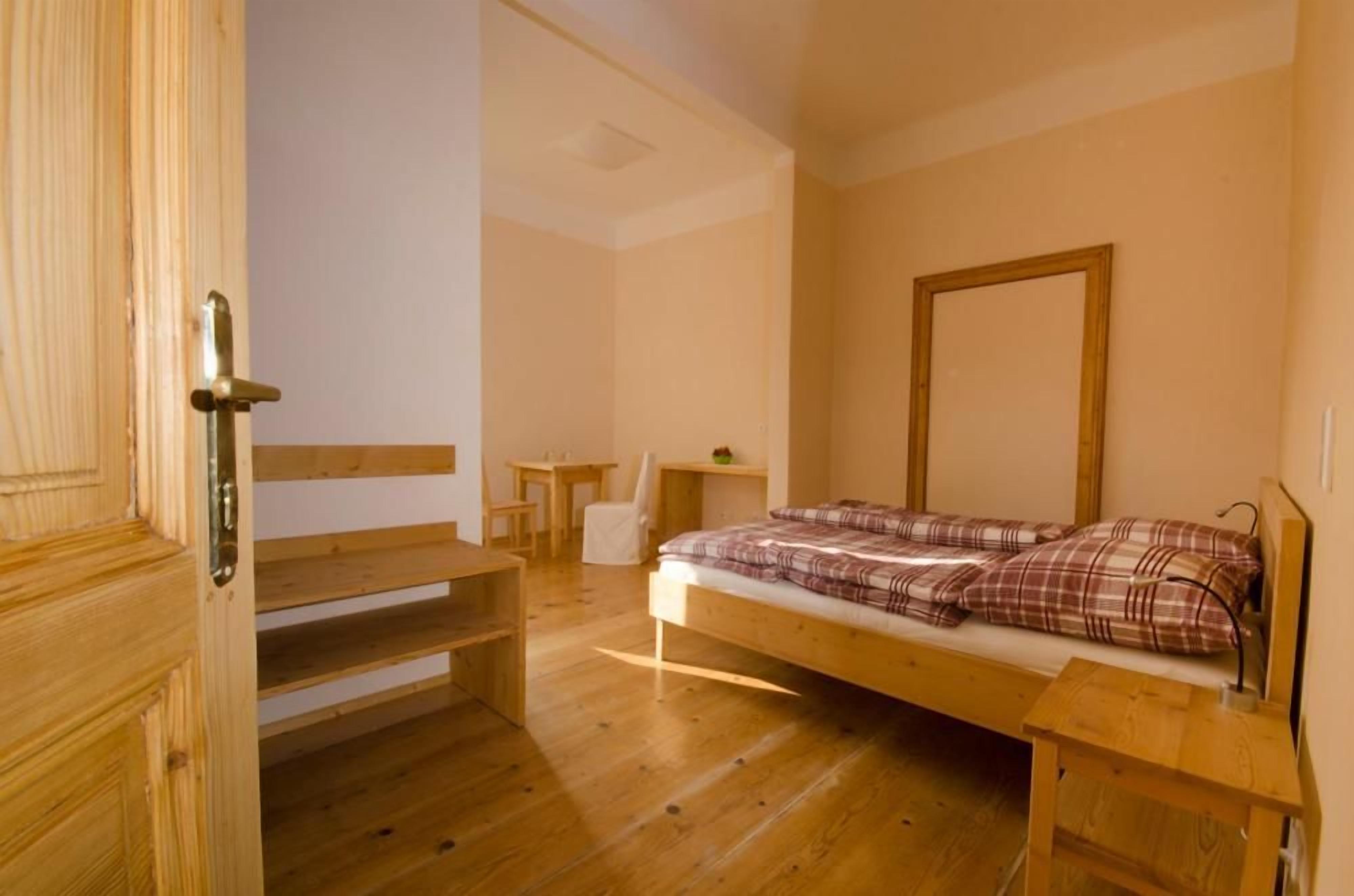 A wooden-framed bed with a plaid blanket, a small wooden table, a chair, and a wooden bench.