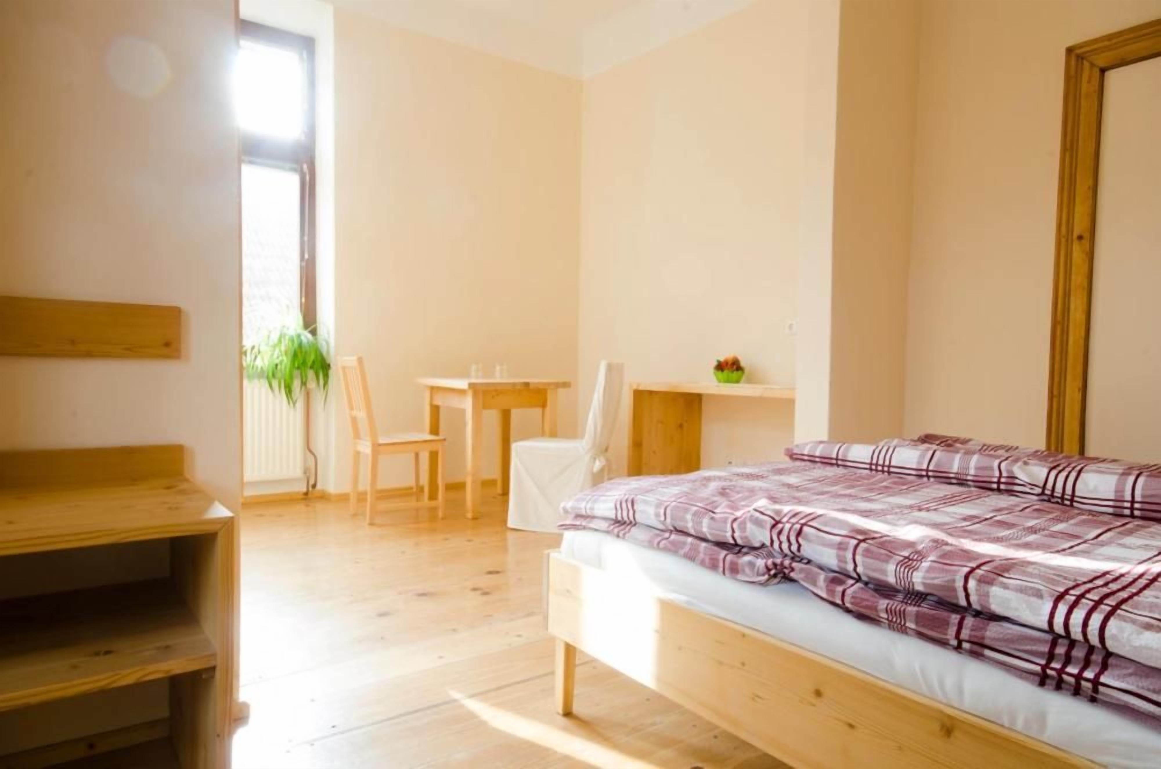 A bedroom with a wooden bed, a desk, a chair, and a small table with a plant.