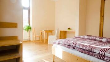 A bedroom with a wooden bed, a desk, a chair, and a small table with a plant.