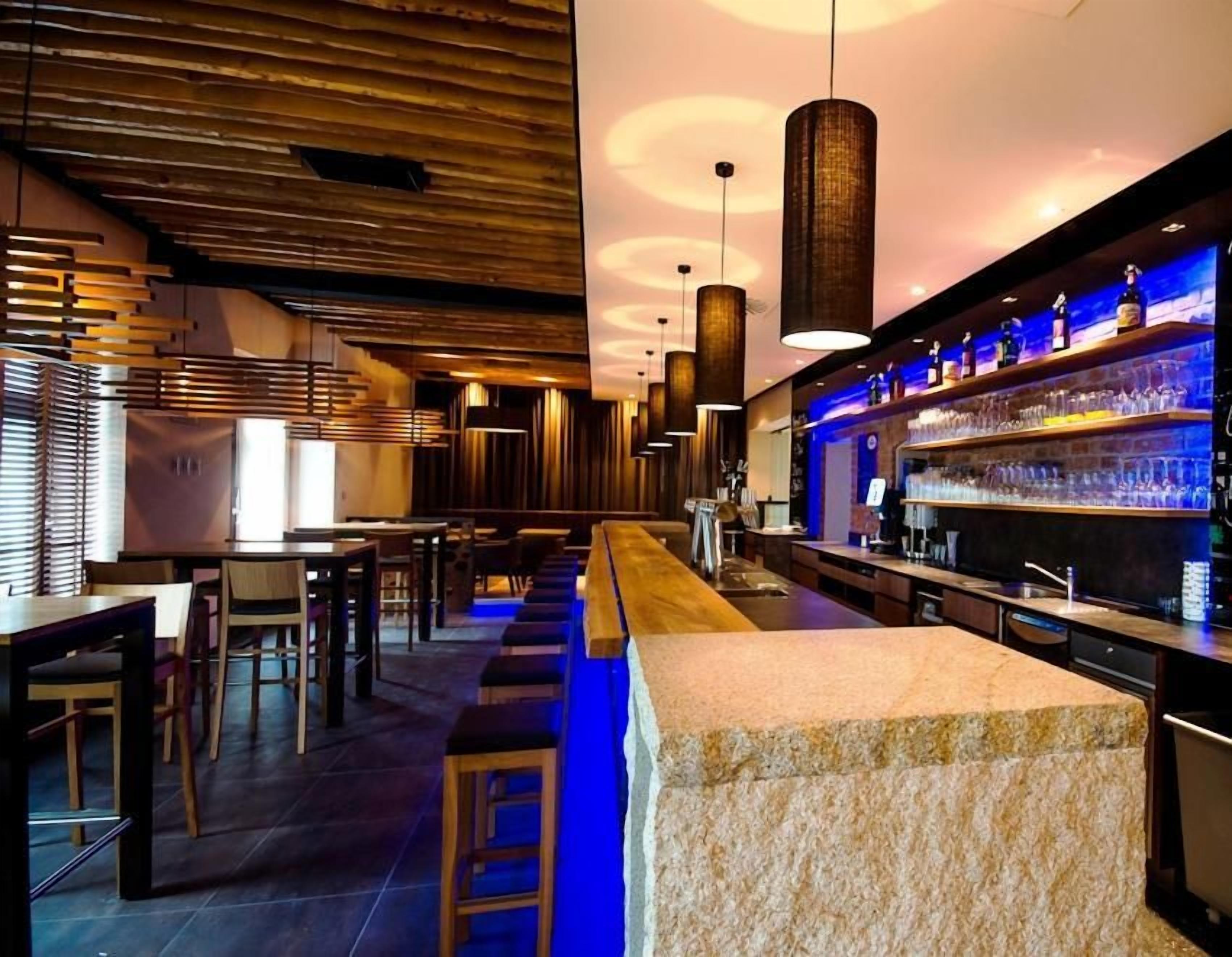 Una zona de bar con una barra larga, taburetes y lámparas colgantes.