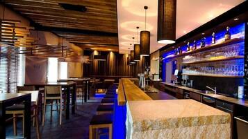 Una zona de bar con una barra larga, taburetes y lámparas colgantes.