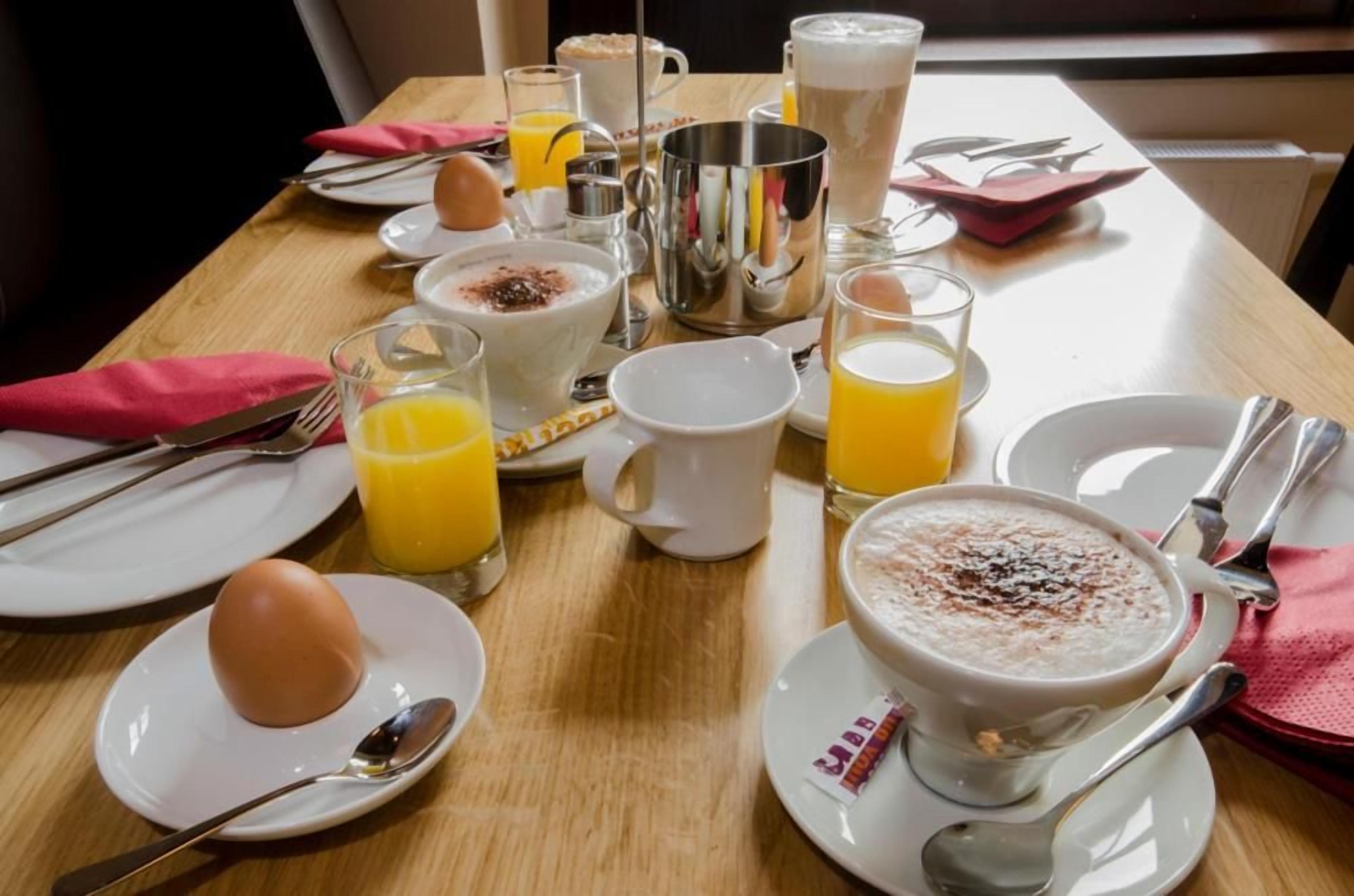 Una mesa de desayuno lista con platos, vasos, una taza y un bol de cereales.
