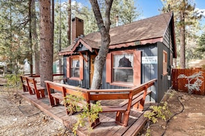 A cabin with a deck and benches, surrounded by trees. - Bear Paw Cottage #2395 (Big Bear Lake)