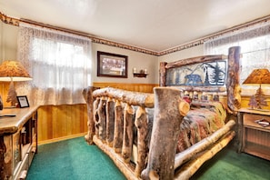 A rustic room with a log bed, wooden walls, and a framed picture of a bear. - Bear Paw Cottage #2395 (Big Bear Lake)