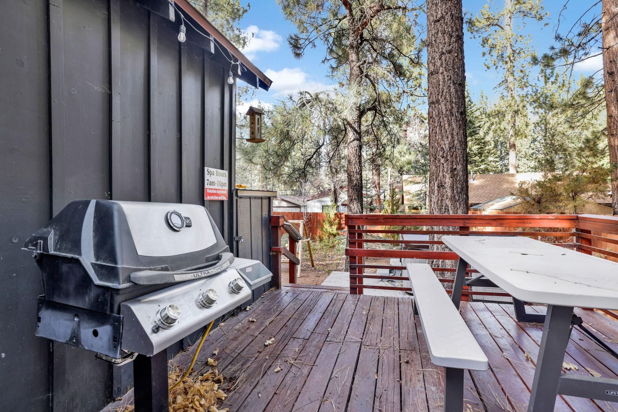 Un área de parrilla exterior con terraza de madera, mesa de picnic y un cartel que indica los horarios del spa.