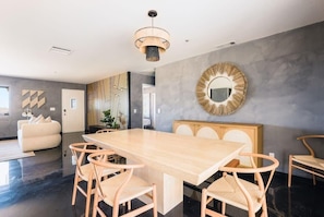 Uma zona de refeições moderna com uma longa mesa de madeira e cadeiras a combinar, um espelho decorativo na parede e um design de parede estampado.