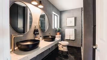 A modern bathroom with a large mirror, two sinks, a toilet, and a shower.