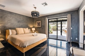 Quarto moderno com cama grande, mesa de cabeceira, abajur e vista para o exterior.
