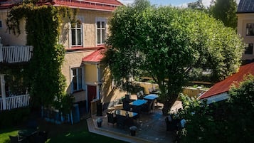 Une cour avec un grand arbre, des sièges extérieurs et un bâtiment doté d’un toit rouge.