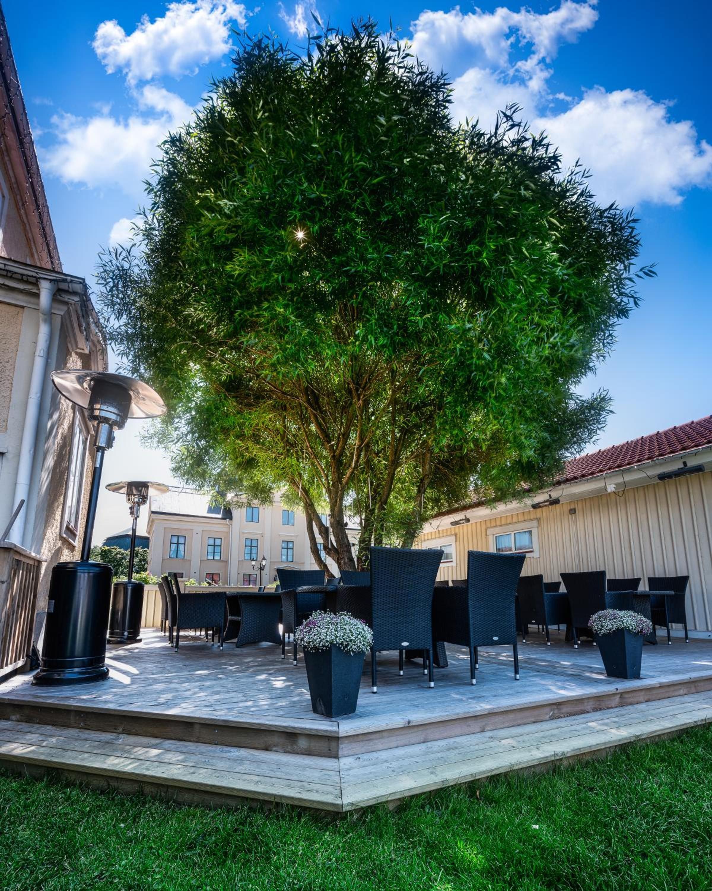 Un espace extérieur aménagé avec des tables et des chaises, entouré d’un arbre et de bâtiments.