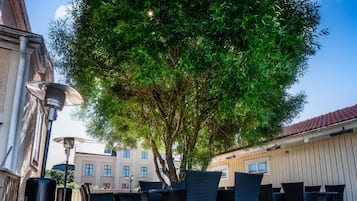 Un espace extérieur aménagé avec des tables et des chaises, entouré d’un arbre et de bâtiments.