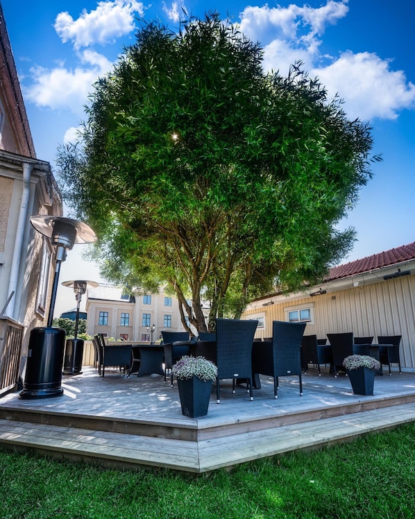 An outdoor seating area with tables and chairs, surrounded by a tree and buildings.