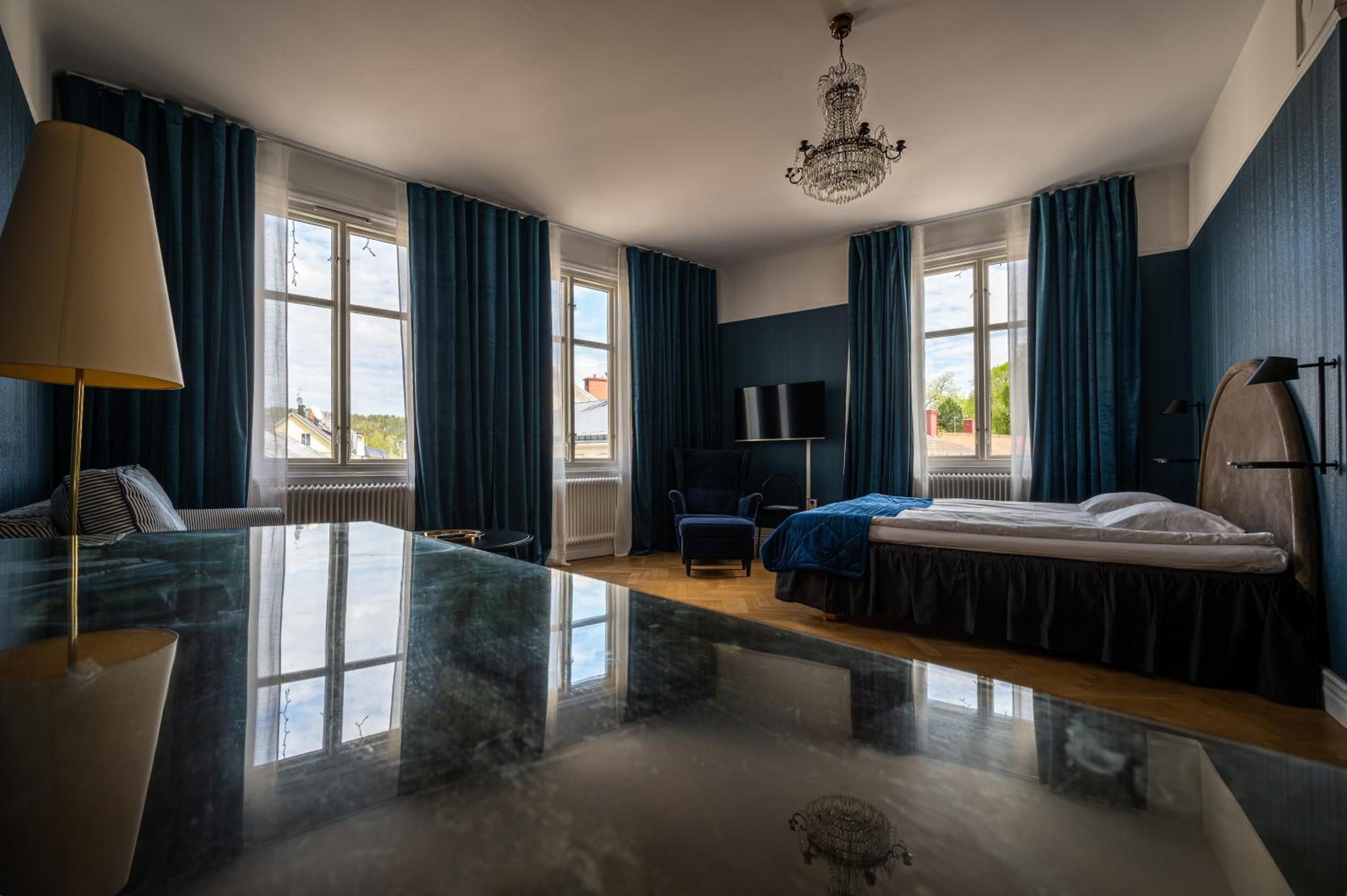 Ett hotellrum med en stor säng, ett skrivbord, en stol, en TV och en kristallkrona.