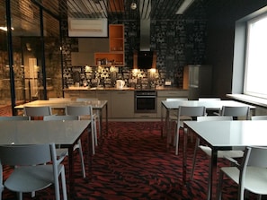 A modern cafe with a black wall featuring coffee-related text, a central coffee bar, and seating areas with tables and chairs. - Loft Car Factory (Warsaw)