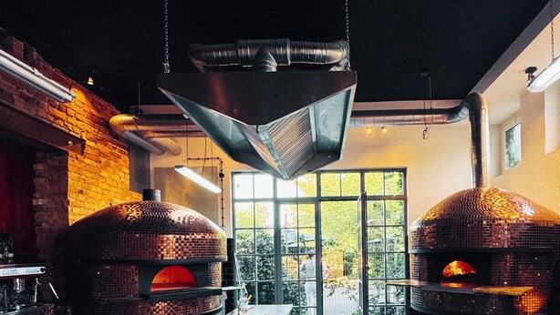 Een keuken met twee bakstenen ovens, een geruit vloertje en een hangende lamp.