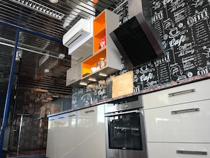 A modern kitchen with stainless steel appliances, a chalkboard wall with coffee-related drawings, and a wooden shelf. - Loft Car Factory (Warsaw)