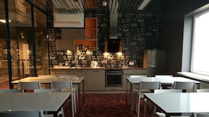 Een modern café met een zwarte muur waarop tekst over koffie staat, een centraal koffiegedeelte en zitgedeeltes met tafels en stoelen.