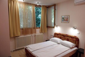 A bedroom with a bed, a window with curtains, a radiator, a wall-mounted light, and a framed picture. - Hostel Oasis (Belgrade)
