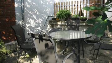 An outdoor patio with a round table and chairs, surrounded by potted plants and a wooden fence.