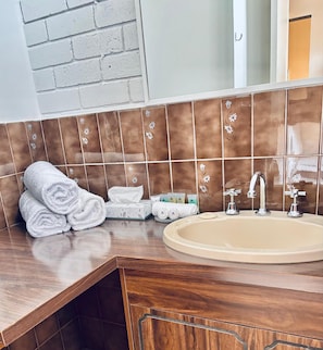A bathroom with a wooden vanity, a beige sink, and a mirror above it.